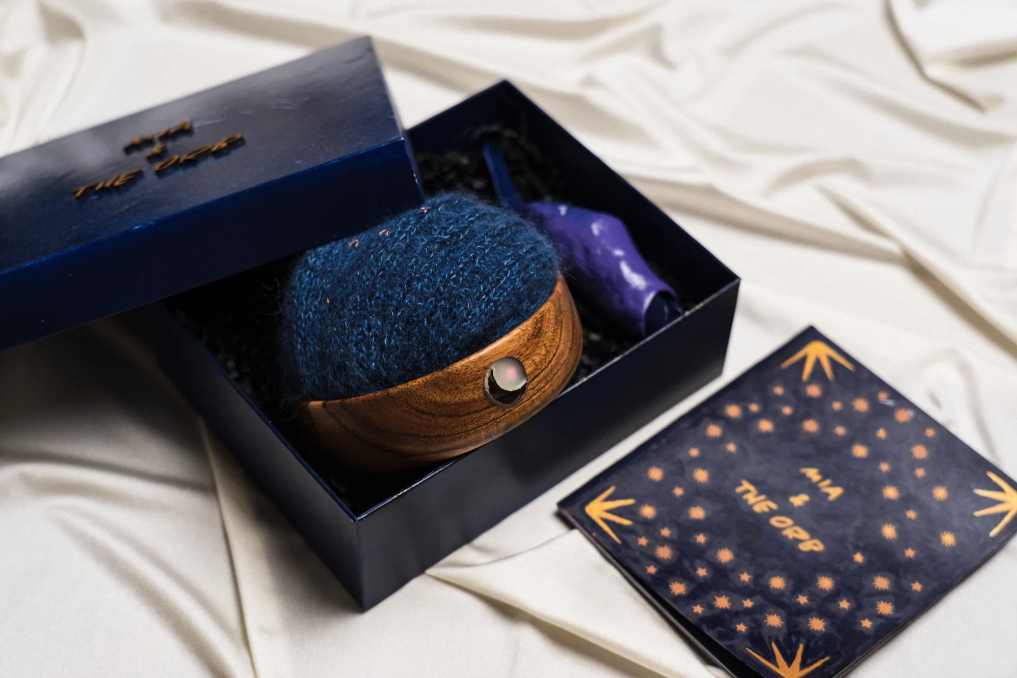 The Mia and the Orb kit in an open navy box: a wooden orb wrapped in blue knitted wool, a purple silicone applicator, and a star-patterned booklet