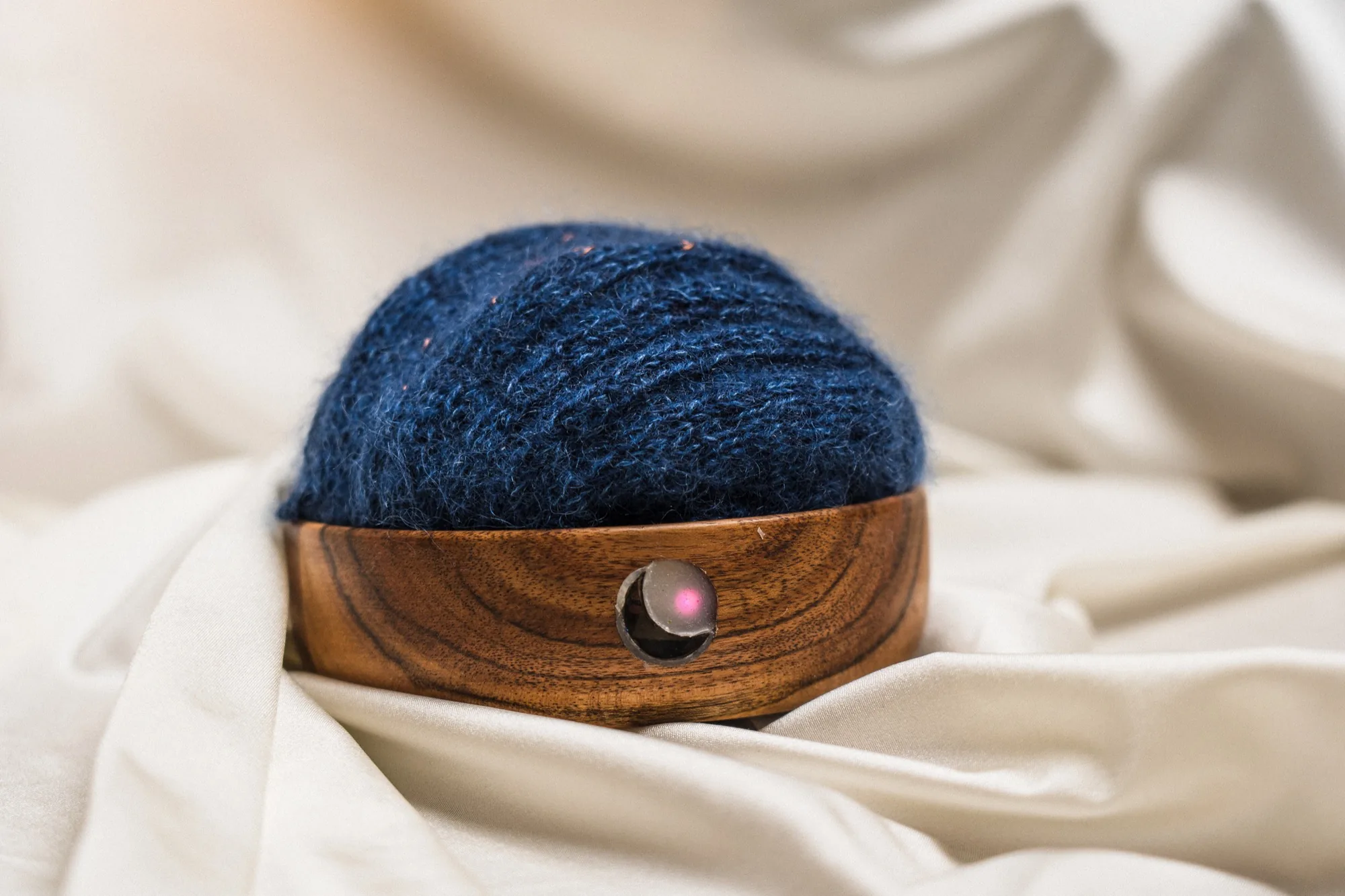 Close-up of the wooden orb wrapped in blue knitted wool, with a small lit indicator set into the wood