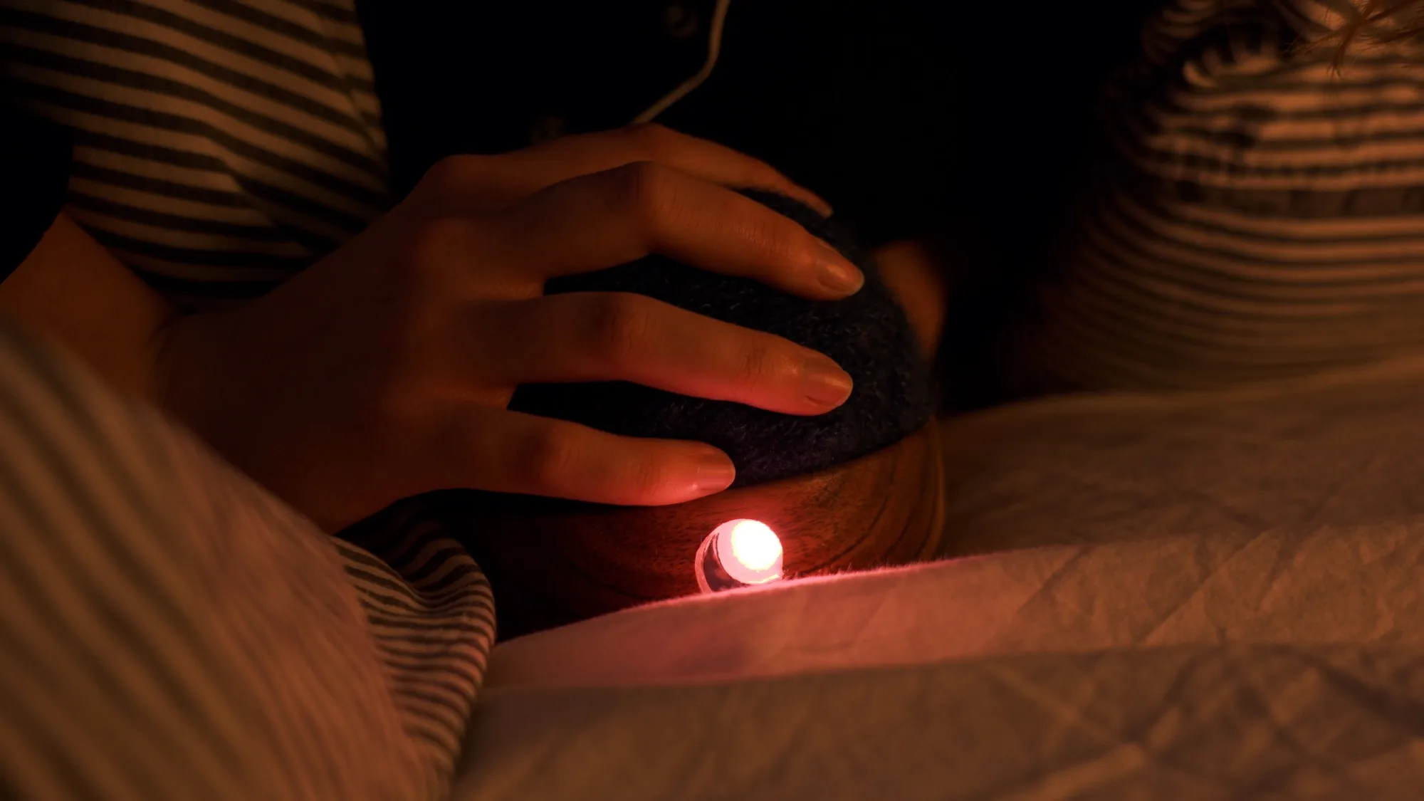 The orb glowing warm red in the dark, held in both hands on a bed at night